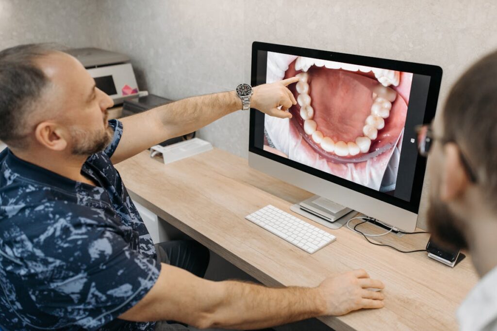 Dentist Sitting by Desk and Showing Teeth on Screen