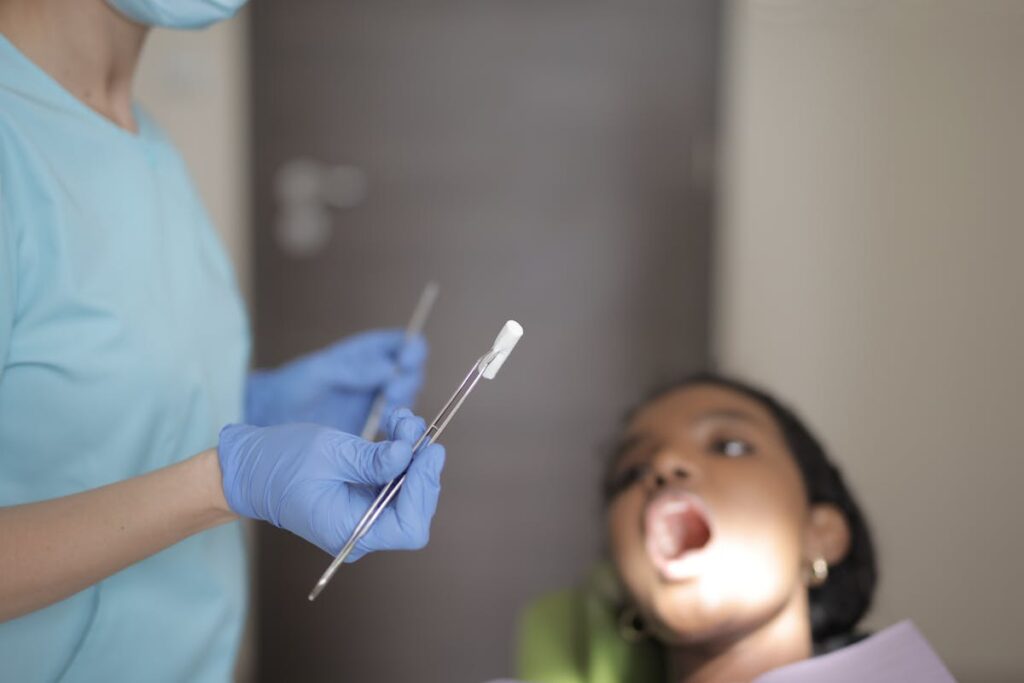 Unrecognizable crop dentist in latex gloves holding instruments while examining teeth of patient in clinic