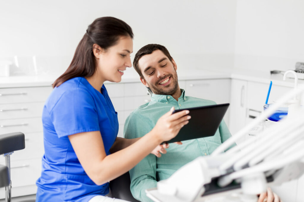 medicine, dentistry and healthcare concept - female dentist with tablet pc computer and male patient discussing teeth treatment at dental clinic office