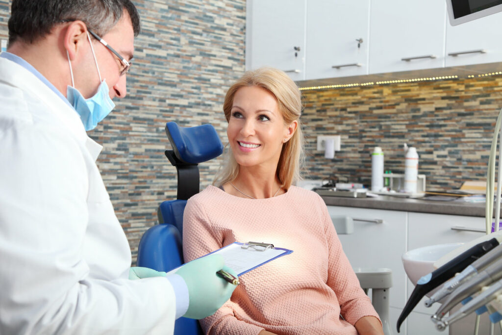 Portrait of executive dentist holding in his hand a clipboard and consultin with beautiful patient at dentist office.