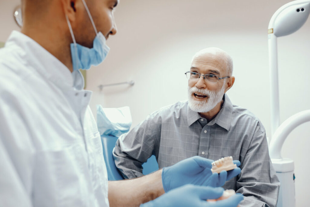 Handsome old man talking to the dendist. Two men in the dentist's office. The doctor shows the patient dentures