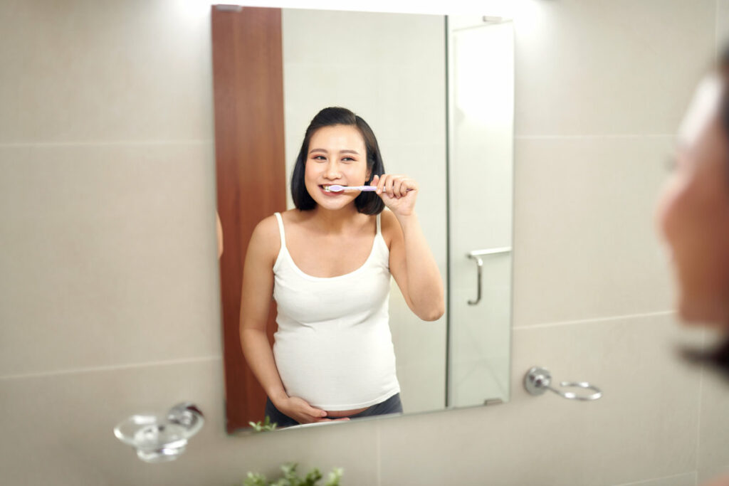 Young pregnant woman brushing teeth in bathroom
