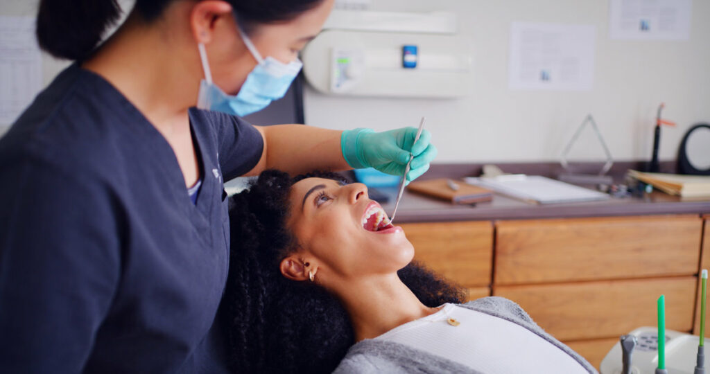 Dentist, patient and inspection with mouth mirror for teeth assessment, oral exam and appointment in office. Dental care, specialist and women with tools for cavity check, gum health and consultation.